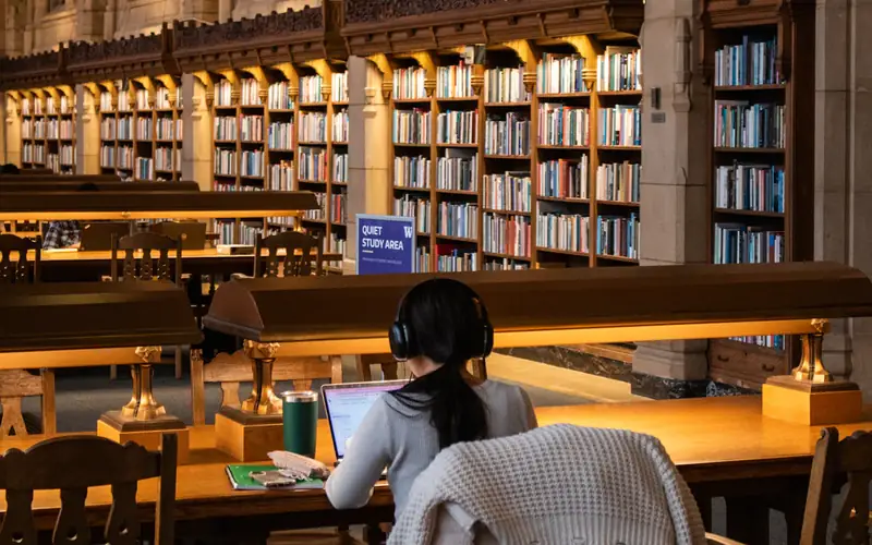 A student at a desk in a warmly lit library